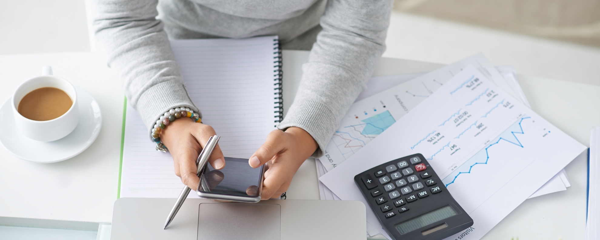Woman at desk with phone, laptop, calculator, and financial documents